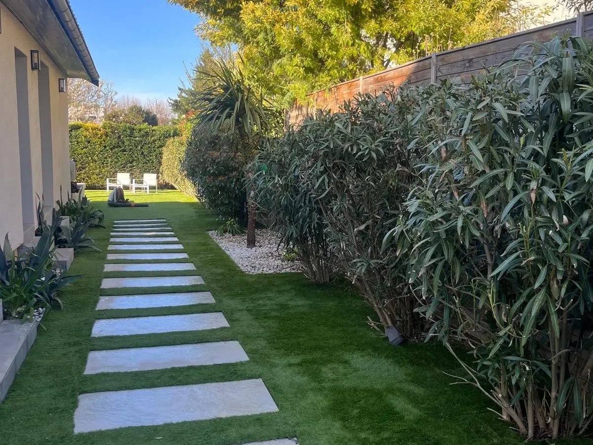 Allée de dalles dans un jardin étroit, entre gazon et haies persistantes